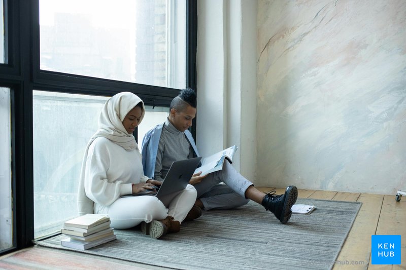 An image of two students sitting next to a window while studying
