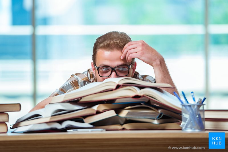 Student peers out from behind a mountain of books